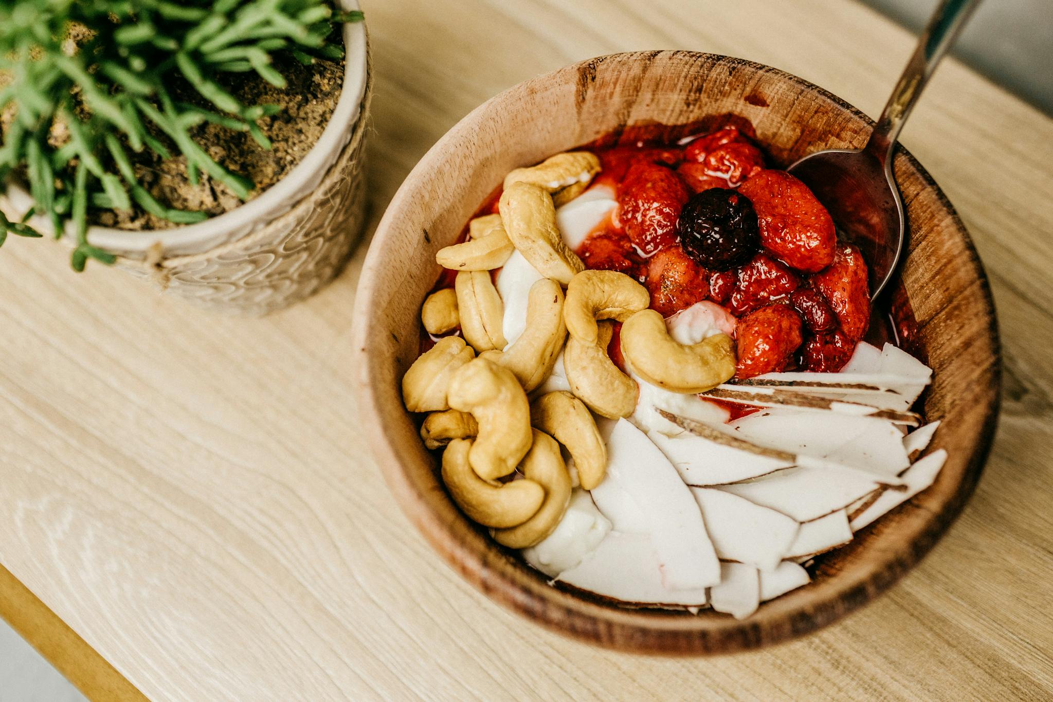 Healthy breakfast bowl with cashews, berries, and coconut slices in a wooden bowl.